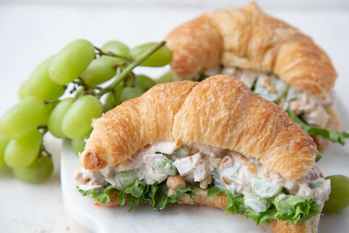 two croissants filled with chicken salad and lettuce, next to a bunch of green grapes.