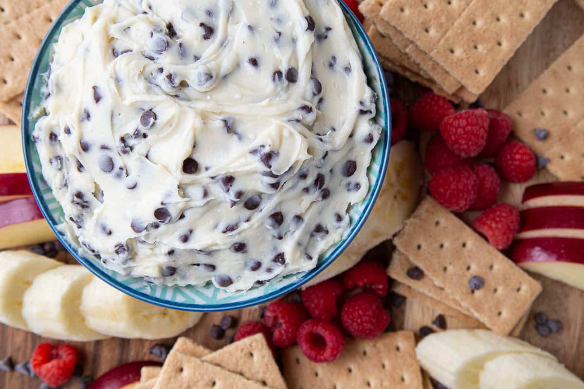 chocolate chip dip with cream cheese in a bowl surrounded by graham crackers and fresh fruit.