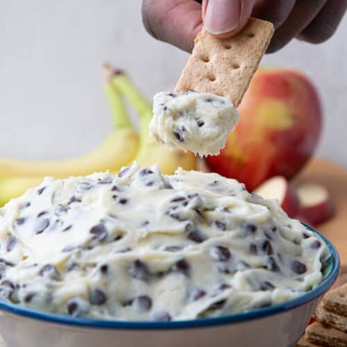 hand holding a graham cracker and dipping it into a bowl of chocolate chip dip.