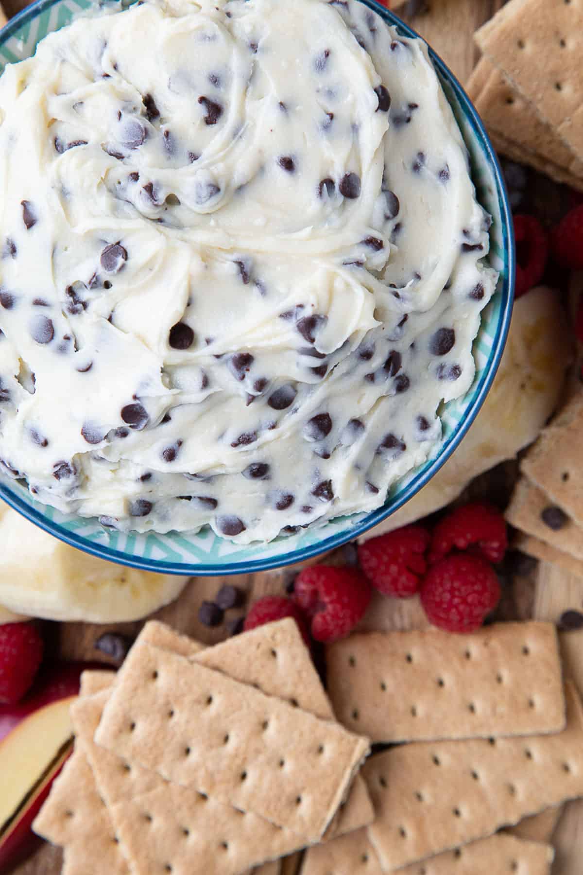 chocolate chip dip in a bowl surrounded by graham crackers, banana slices, and raspberries.