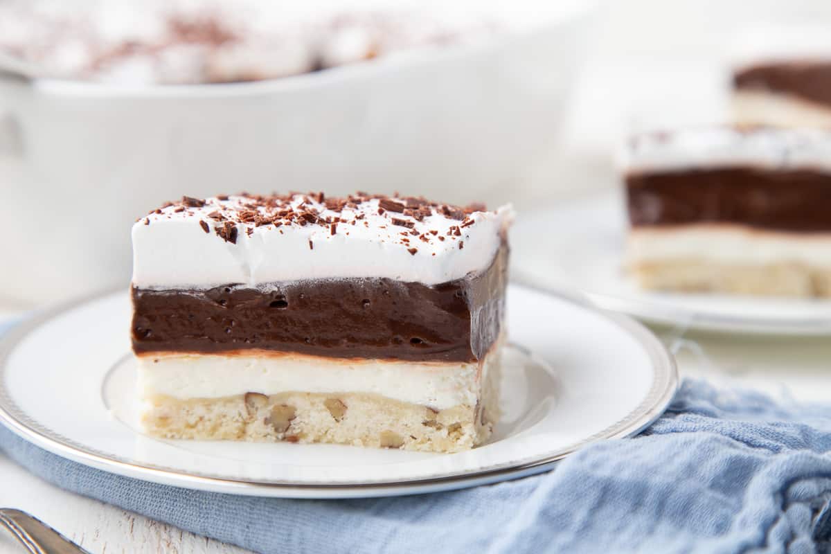 two slices of chocoalte delight on white plates, on top of a blue napkin.