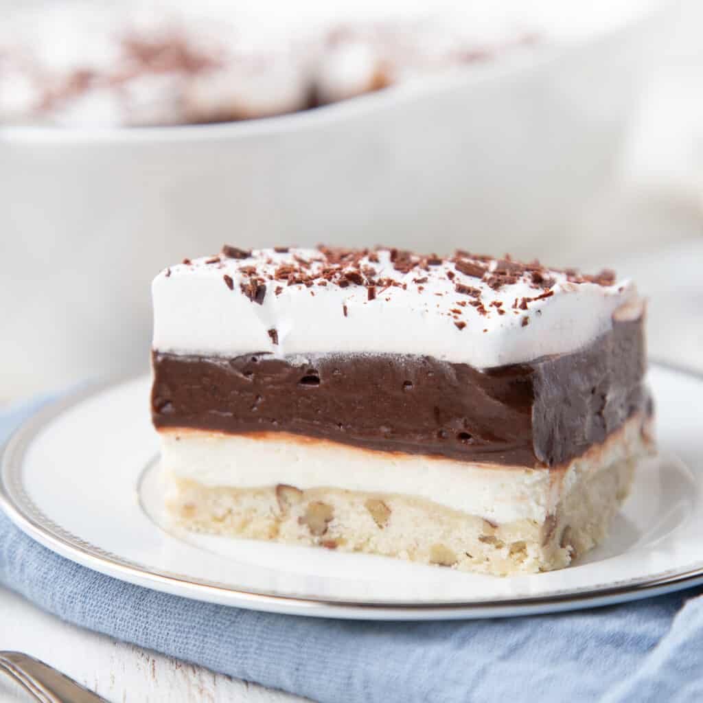 piece of chocolate delight layered dessert on a white plate on top of a blue napkin.