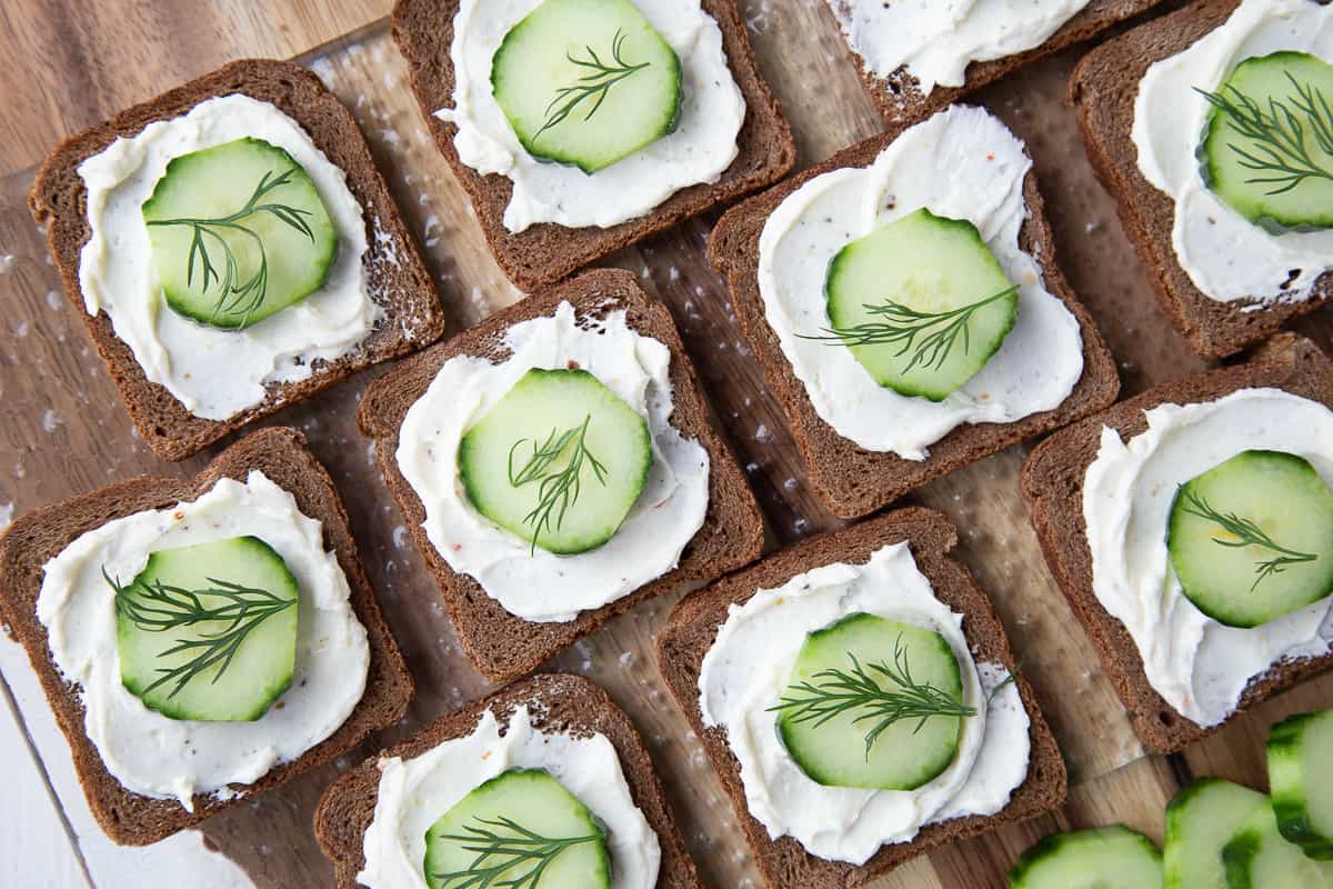 mini cucumber sandwiches on a wooden board, each topped with fresh dill.