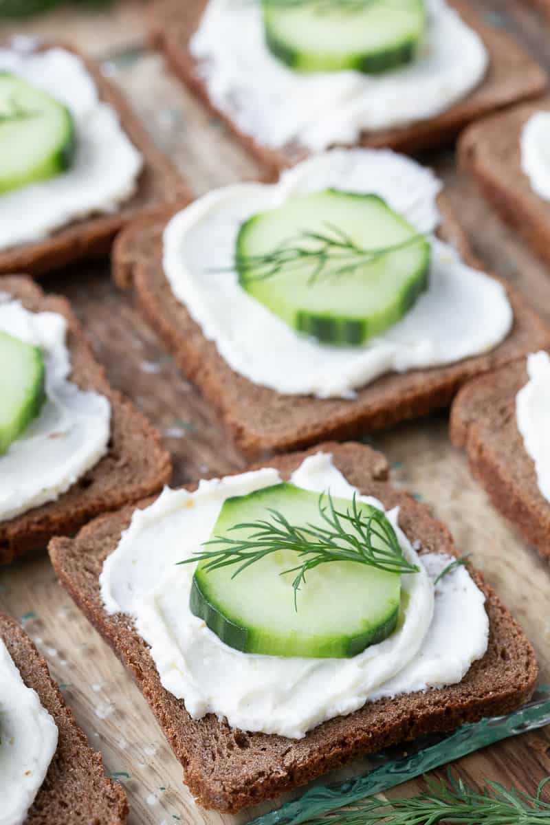 mini pumpernickel bread topped with cream cheese and a cucumber slice, topped with a sprig of fresh dill.