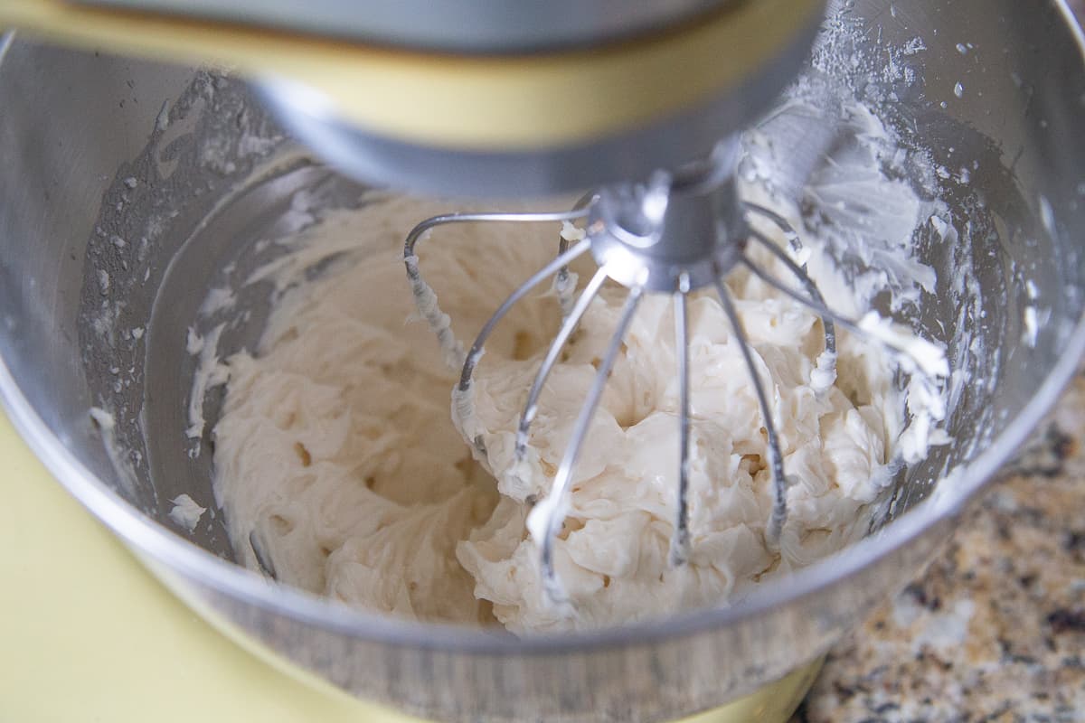 yellow stand mixer with a whisk attachment beating a creamy butter and sugar mixture.