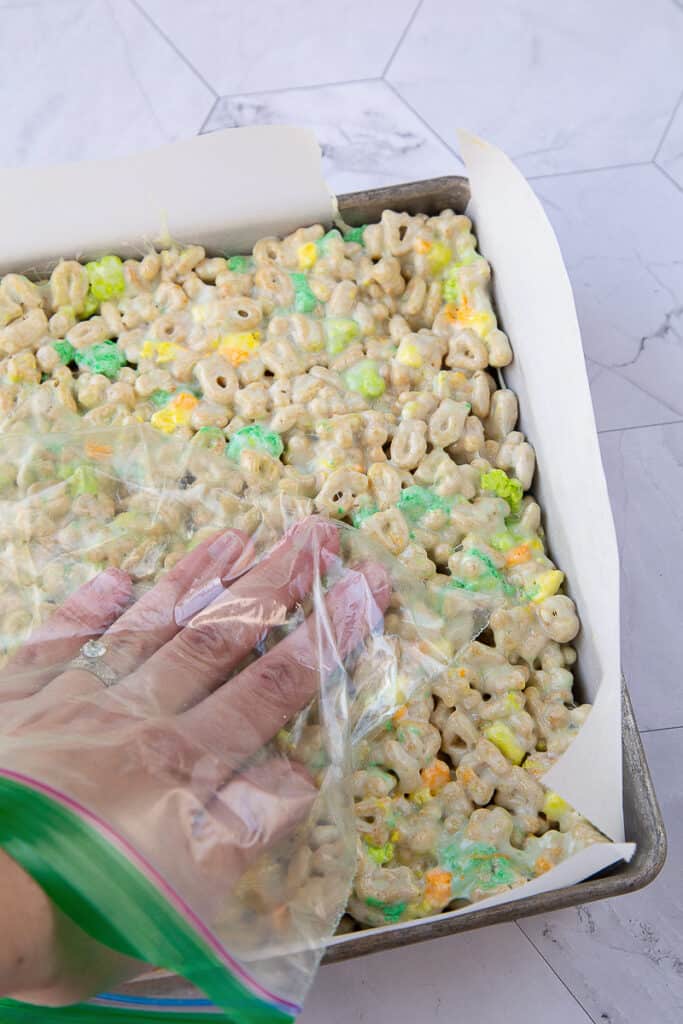 hand inside a plastic bag pressing marshmallow treats into a pan.