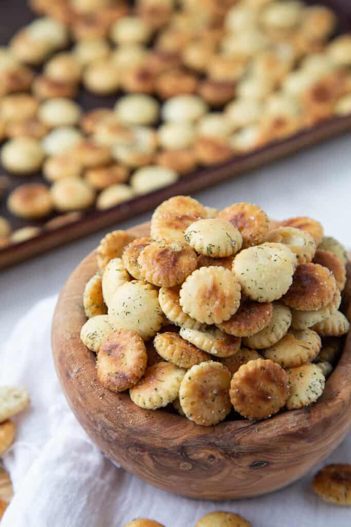 ranch oyster crackers in a wooden bowl with a sheet pan of oyster crackers in the background.