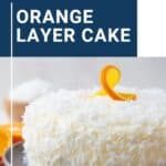 orange layer cake on a gray platter, topped with coconut and an orange garnish.