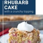 slice of rhubarb cake on a white plate, topped with whipped cream.
