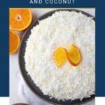 orange layer cake on a gray platter, topped with coconut and an orange garnish.