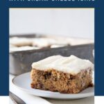 banana cake with cream cheese frosting on a white plate next to a napkin and fork.