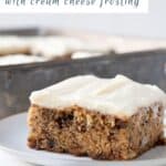 banana cake with cream cheese frosting on a white plate next to a napkin and fork.