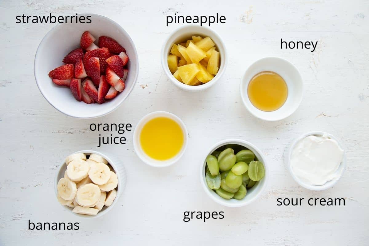 assorted fruit, sour cream, and honey in ramekins on a white table.