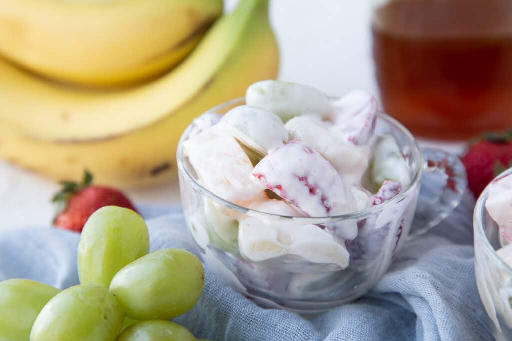 creamy fruit salad in a glass cup, surrounded by grapes, bananas, and honey.