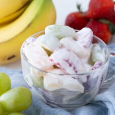 creamy fruit salad in a glass dish, surrounded by fresh fruit.