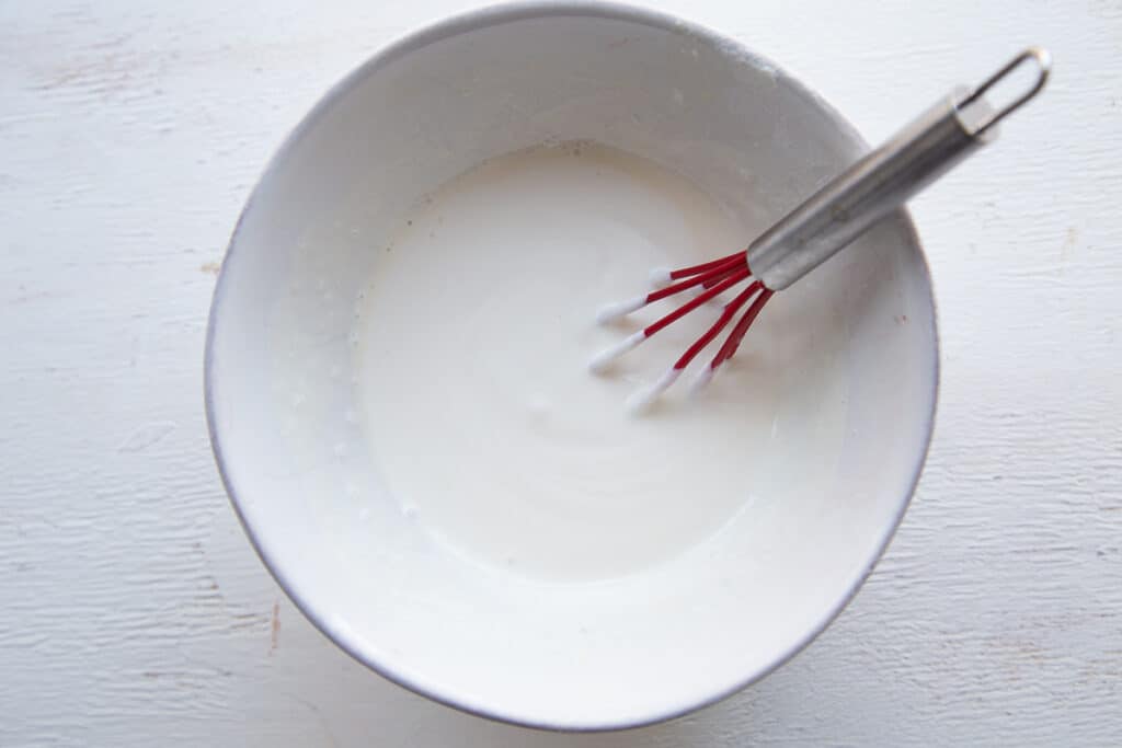 sour cream dressing for fruit salad in a white bowl with a mini red whisk.