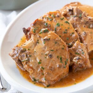 crock pot pork chops in sauce on a white oval platter.