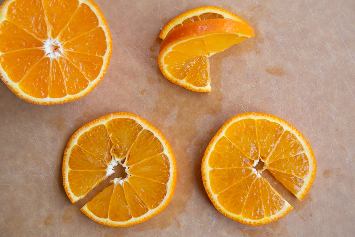 slices of orange on a cutting board showing how to make an orange garnish.