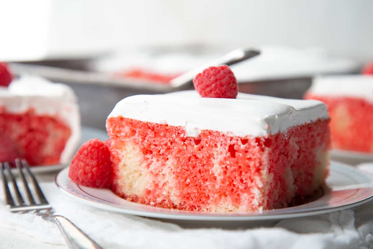 slice of raspberry jello poke cake on a white plate with a fork nearby.