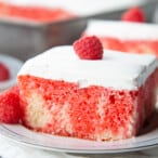 red jell-o poke cake topped with whipped cream and raspberry on a white china plate.