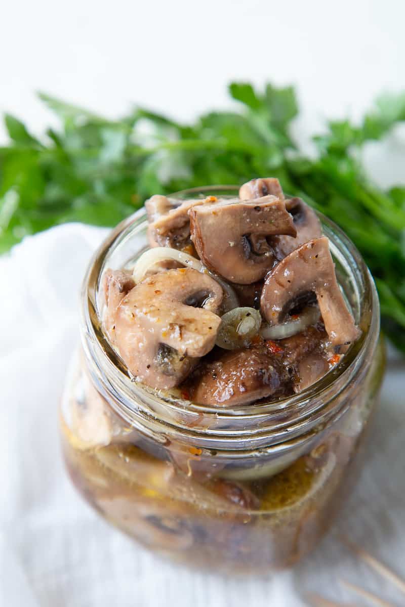 glass jar filled with marinated mushrooms with fresh parsley in the background.