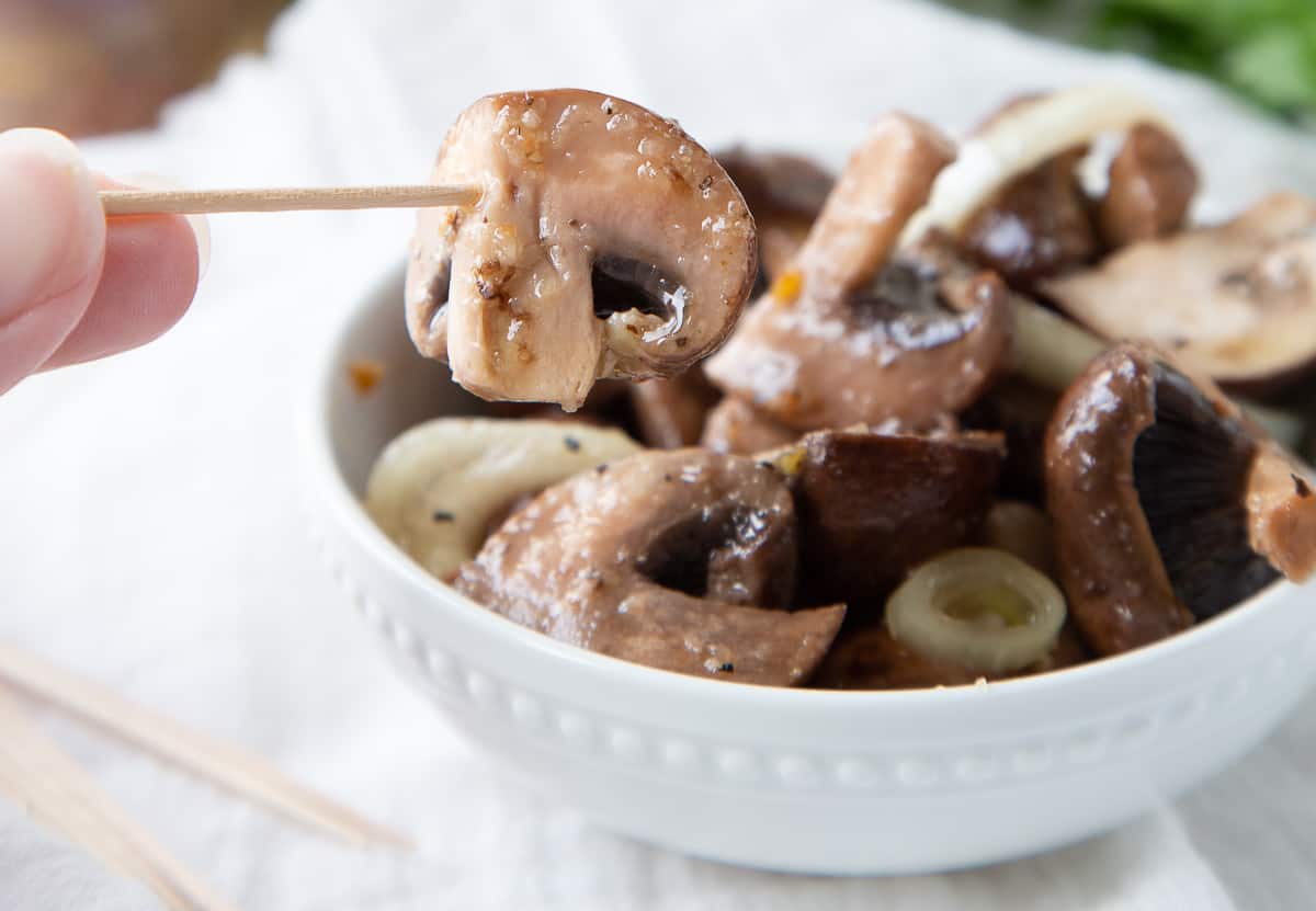 hand holding a toothpick picking up a marinated mushroom.