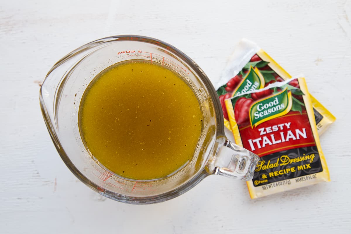 glass pitcher with italian dressing, next to two packets of italian dressing mix.