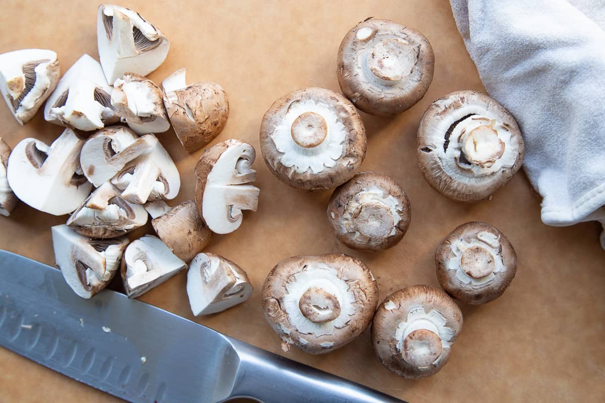 baby bella mushrooms on a cutting board with a knife.