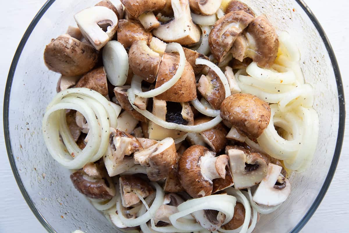 mushrooms and onion coated with dressing in a glass bowl.