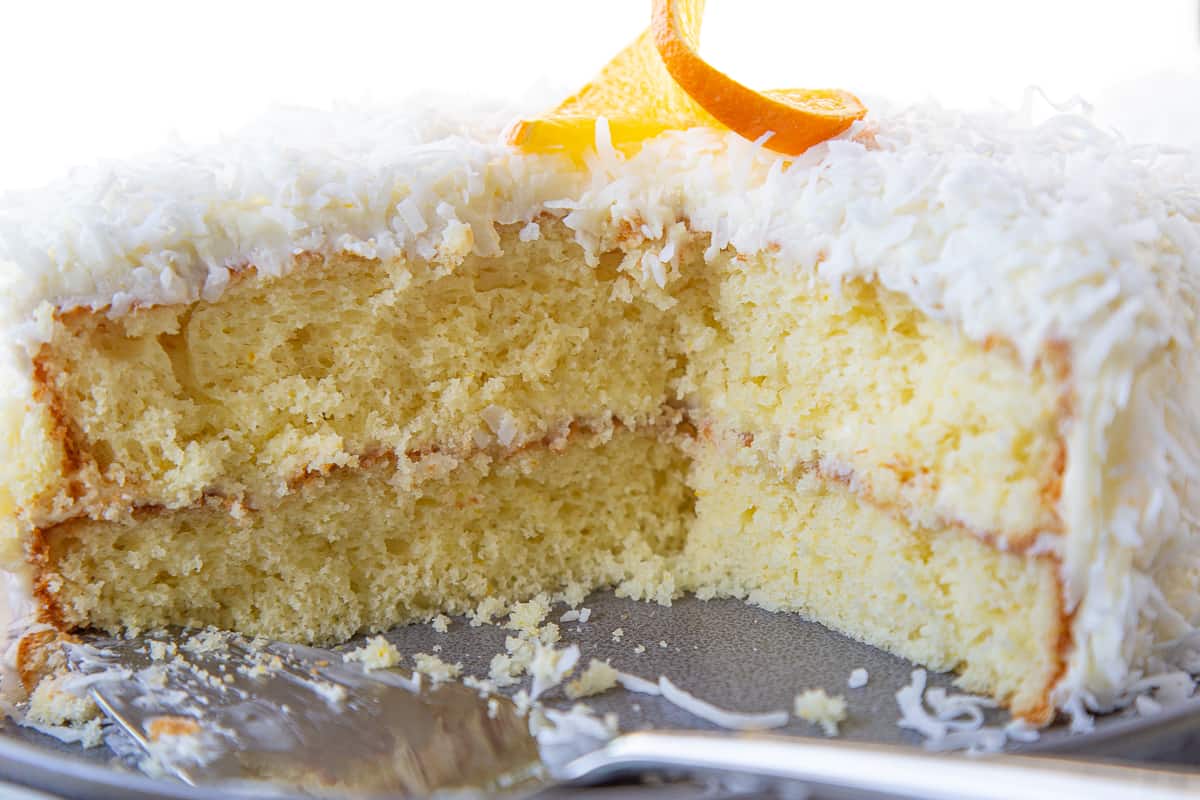 cross section of an orange layer cake topped with coconut and an orange garnish.