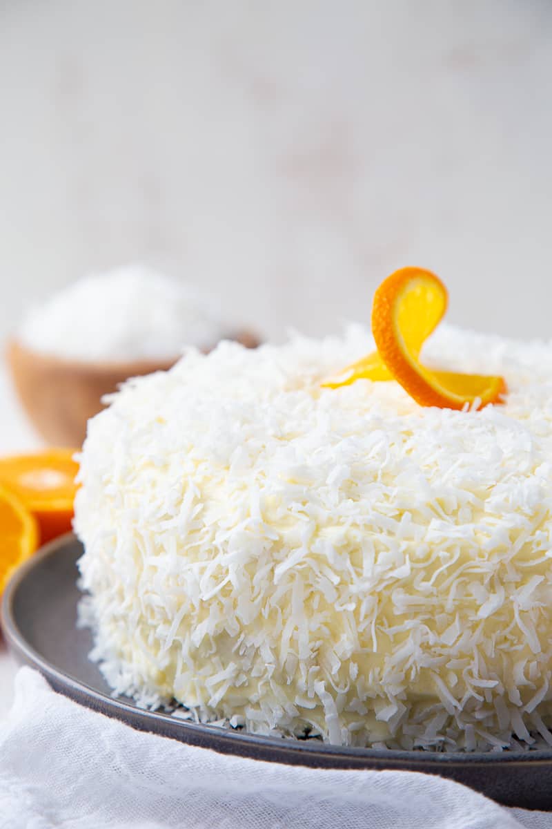 orange layer cake topped with coconut and an orange slice garnish.
