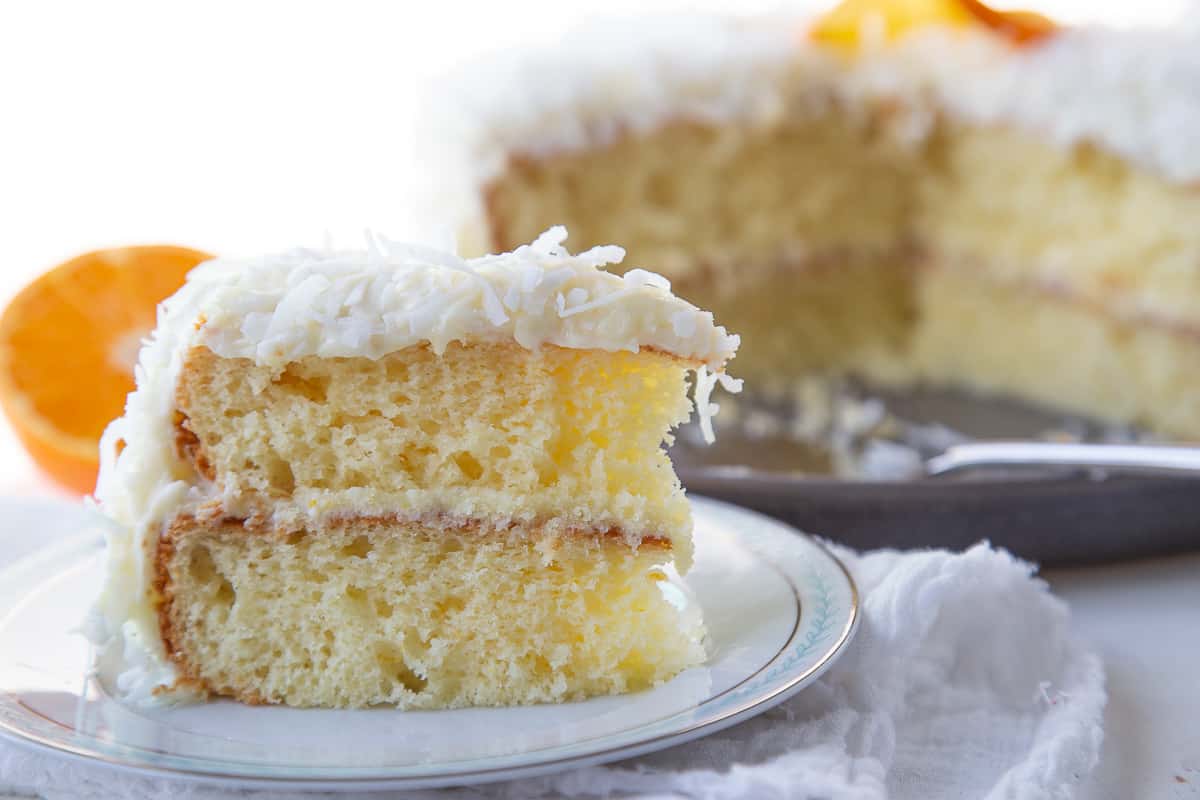 slice of orange cake standing upright on a china plate, with the whole cake in the background.