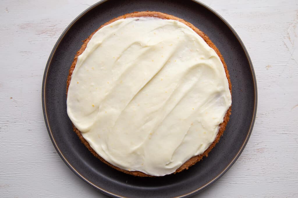 one layer of orange cake on a gray plate, topped with cream cheese frosting.