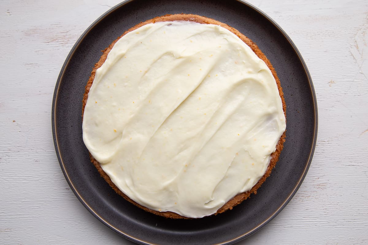 one layer of orange cake on a gray plate, topped with cream cheese frosting.