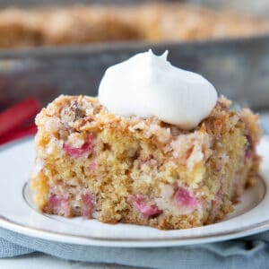 slice of rhubarb cake on a white plate topped with whipped cream.