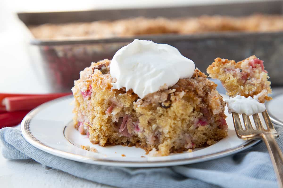 slice of rhubarb cake with whipped cream on top, with a bite taken out.