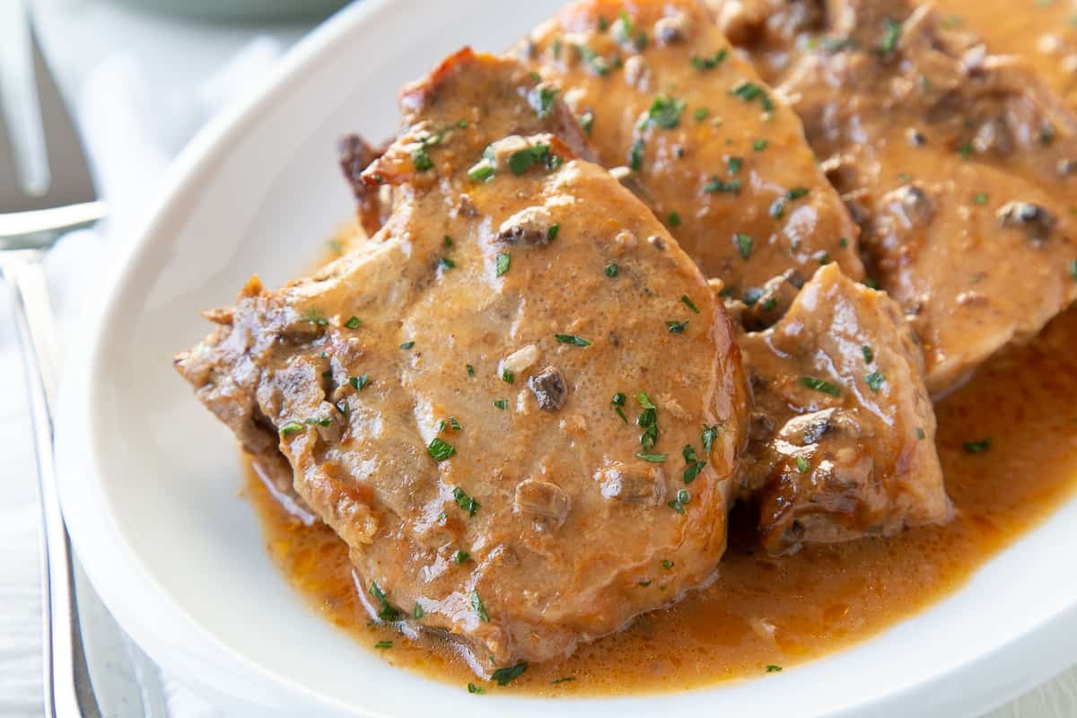 crock pot pork chops on a white oval platter next to a serving fork.