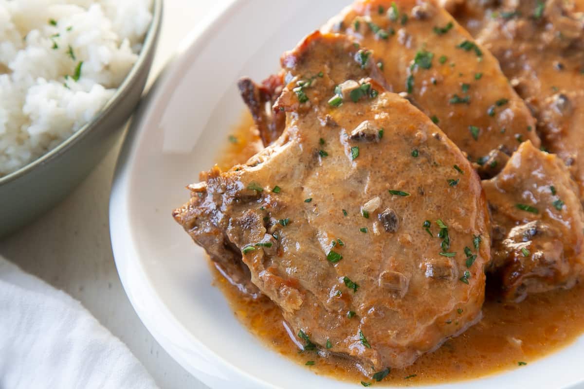 slow cooker pork chops on a white platter with a side of rice in a green bowl.