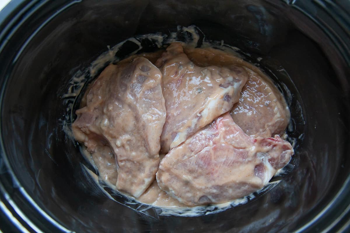 raw pork chops covered in sauce in a crock pot.