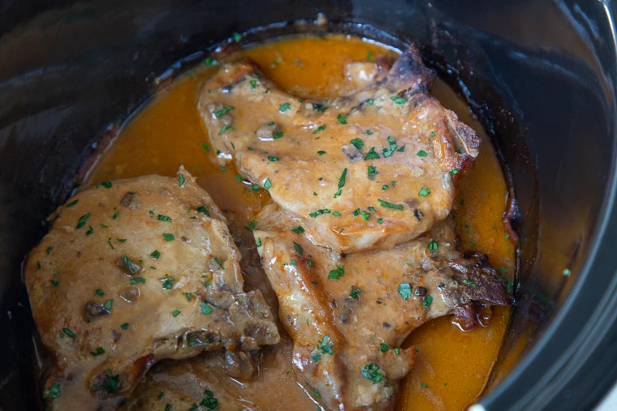cooked pork chops with an orange sauce in a crock pot.