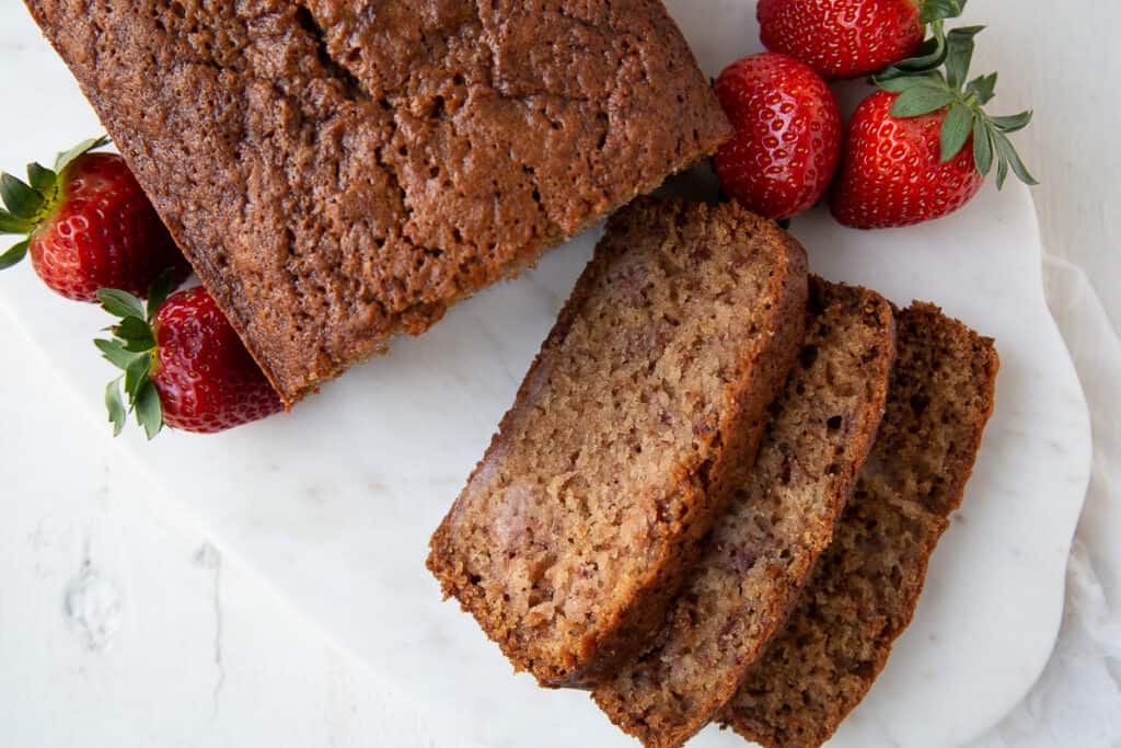 loaf of fresh strawberry bread with slices taken out on a white marble platter.