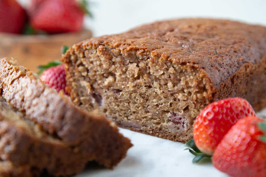 loaf of strawberry bread with a few slices cut out, next to fresh strawberries.