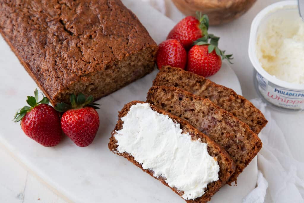 a loaf of strawberry bread with slices cut out, spread with cream cheese.