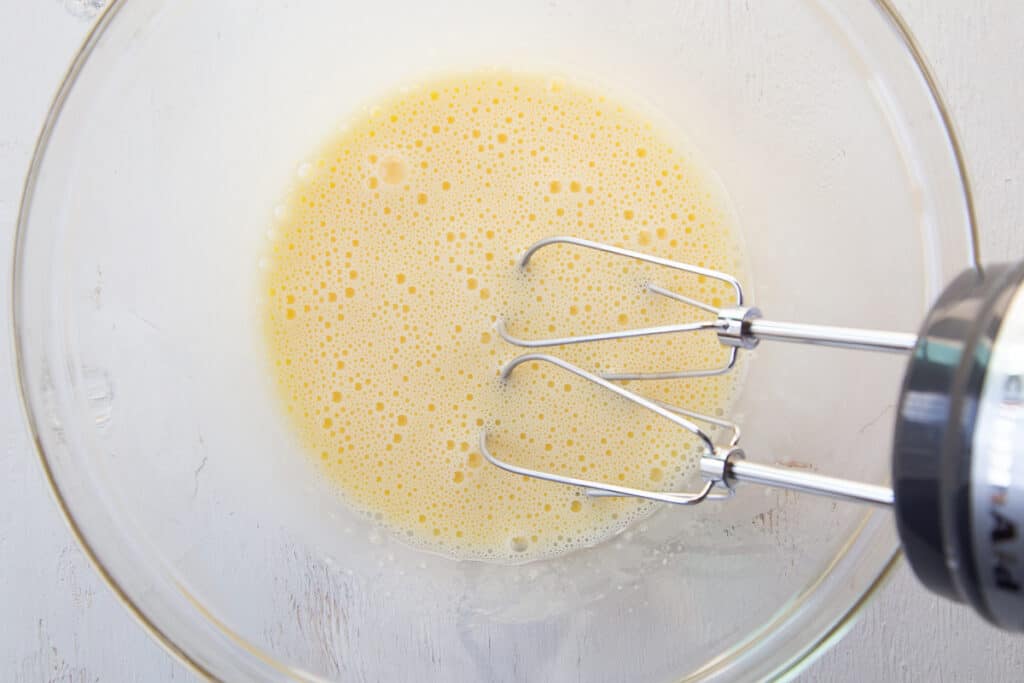 hand mixer mixing eggs and sugar in a glass bowl.