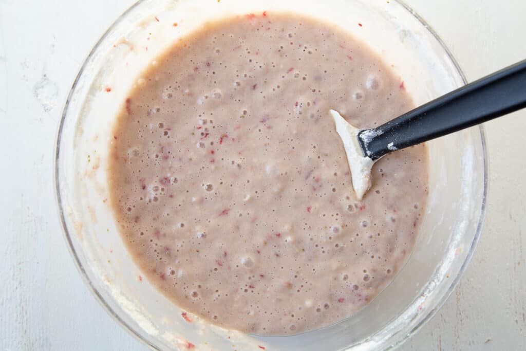 strawberry bread batter in a glass bowl with a spatula.