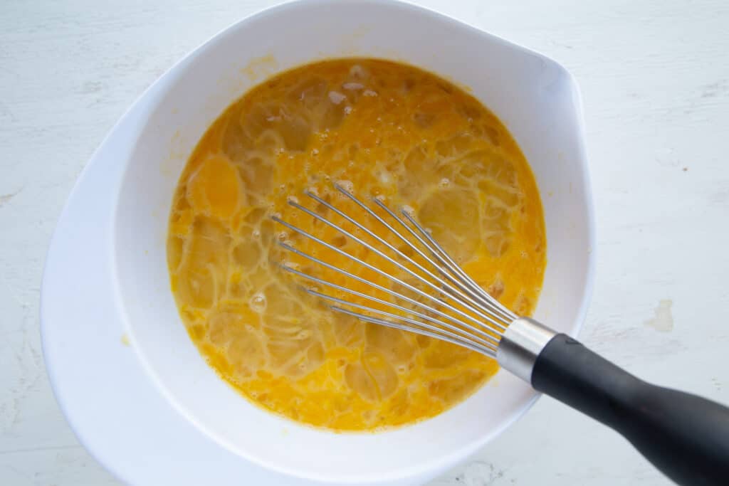 eggs being whisked in a large white bowl.