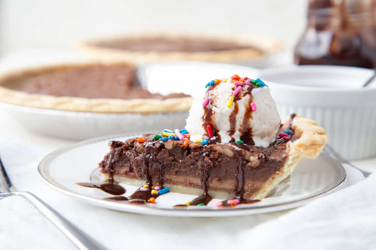 brownie pie slice on a plate, topped with ice cream and sprinkles, with full pies in the background.