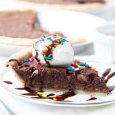 slice of brownie pie topped with ice cream, chocolate sauce, and sprinkles on a white plate.