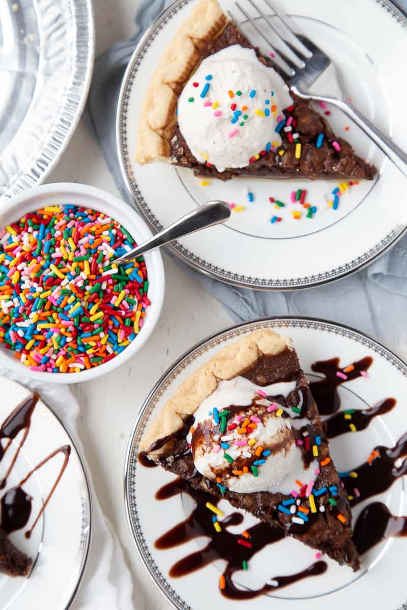 slices of brownie pie on white plates with a bowl of rainbow sprinkles nearby.