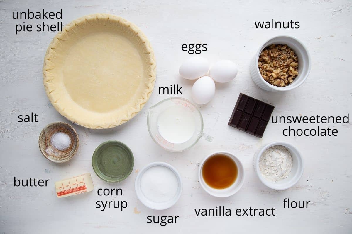 eggs, walnuts, chocolate, milk, sugar, flour and other baking ingredients on a white table.